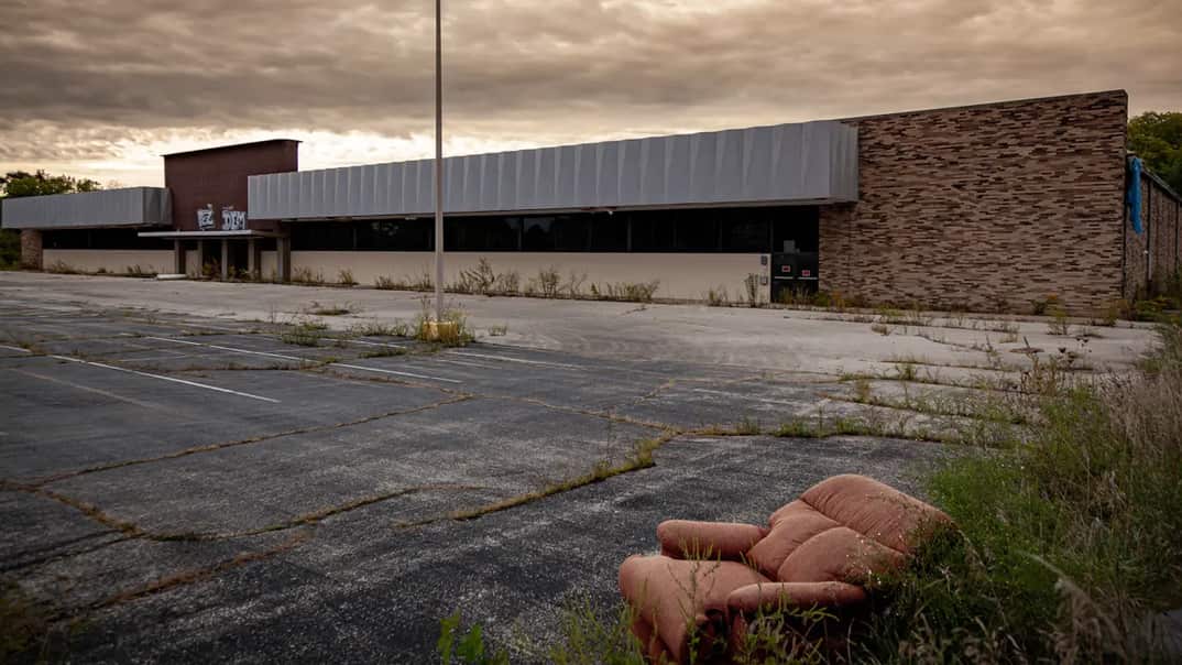 A stuffed chair sits outside a closed business in the empty parking lot