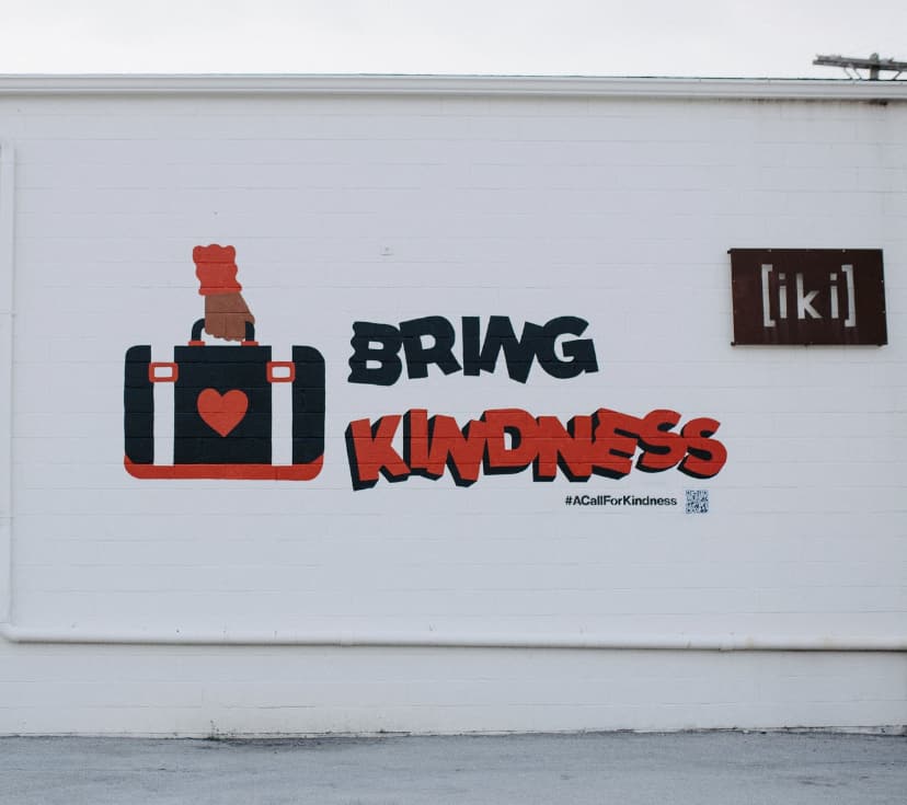 Kindness that reads "Bring Kindness" with a hand holding a suitcase with a heart