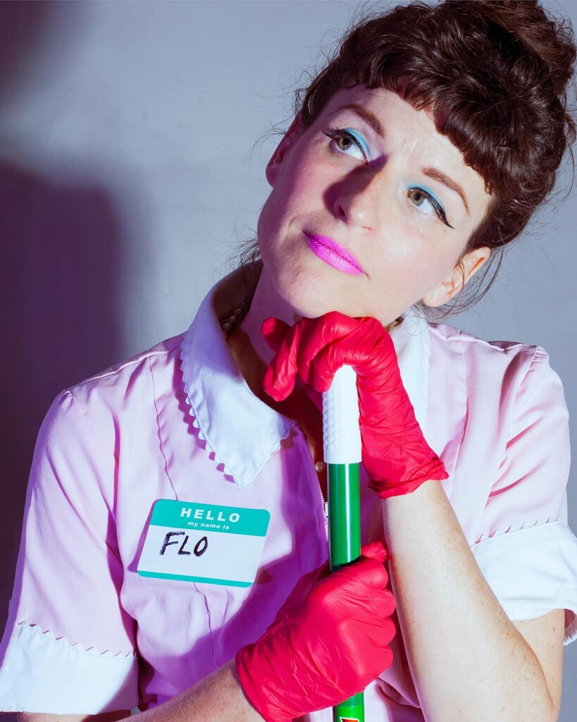 Woman with pink dress, nametag that reads Flo in pink gloves holding a broom